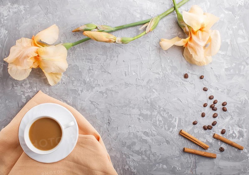 Orange iris flowers and a cup of coffee on a gray concrete background. Morninig, spring, fashion composition. Flat lay, top view, copy space
