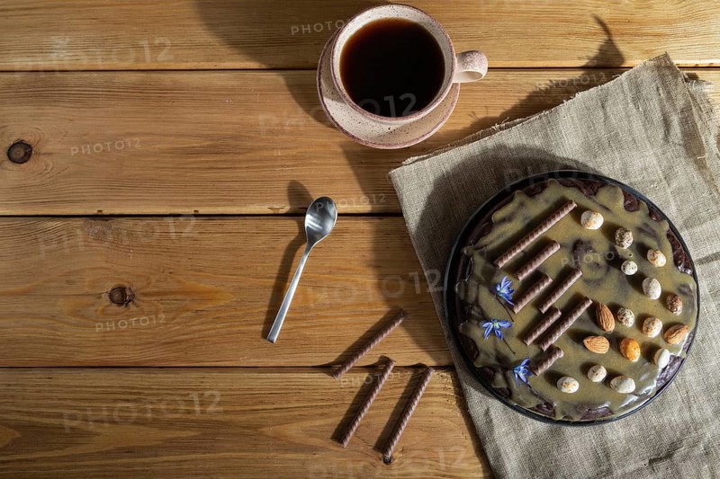Homemade chocolate brownie cake with caramel cream and almonds with cup of coffee on wooden background and linen textile. Top view, hard light, copy space, flat lay