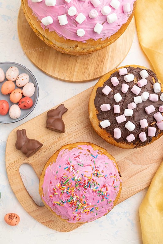 Homemade glazed and decorated easter pies with chocolate eggs and rabbits on a white concrete background and yellow textile. top view, flat lay, close up