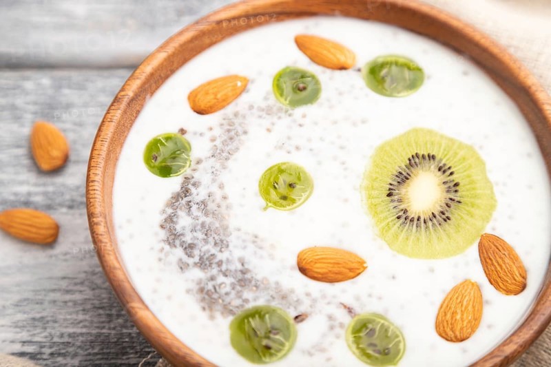 Yogurt with kiwi, gooseberry, chia and almonds in wooden bowl on gray wooden background and linen textile. Side view, close up, selective focus
