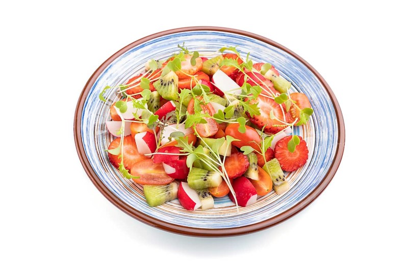 Vegetarian fruits and vegetables salad of strawberry, kiwi, tomatoes, microgreen sprouts isolated on white background. Sideview, close up