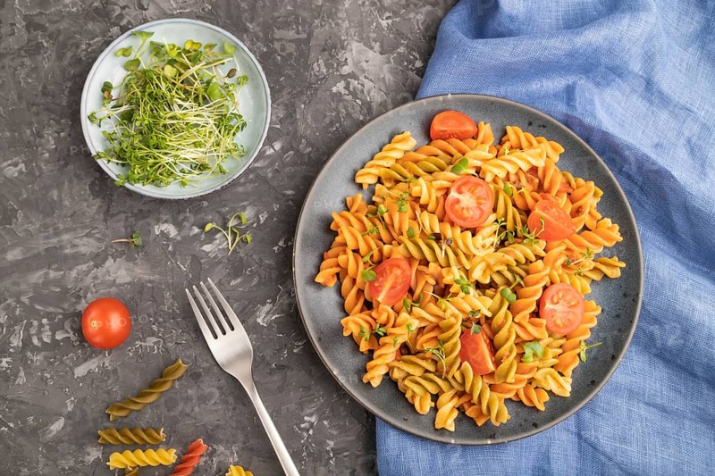 Tortiglioni semolina pasta with tomato and microgreen sprouts on a black concrete background and blue textile. Top view, flat lay, close up