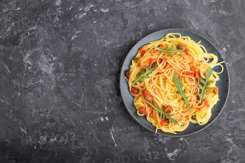 Corn noodles with tomato sauce and arugula on a black concrete background. Top view, flat lay, copy space