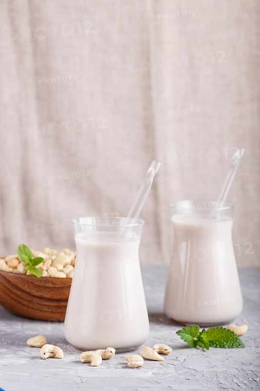 Organic non dairy cashew milk in glass and wooden plate with cashew nuts on a gray concrete background. Vegan healthy food concept, close up, side view