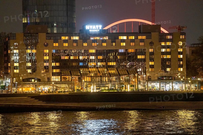 The Hyatt Regency Hotel on the Rhine, in Cologne Deutz, behind it the illuminated arch of the Lanxess Arena, Rhine, North Rhine-Westphalia, Germany, Europe