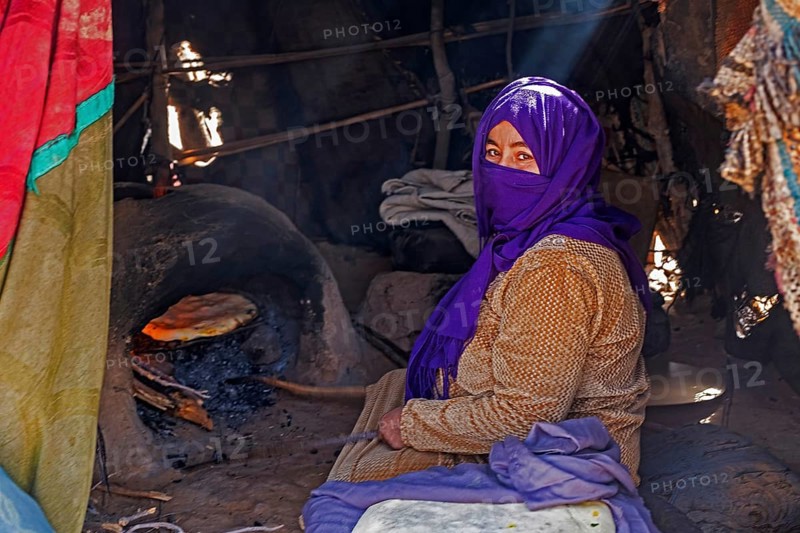 Nomadic Bedouin woman with hijab baking bread in traditional oven in tent in the Sahara Desert near Merzouga, Drâa-Tafilalet, Errachidia, Morocco, Africa