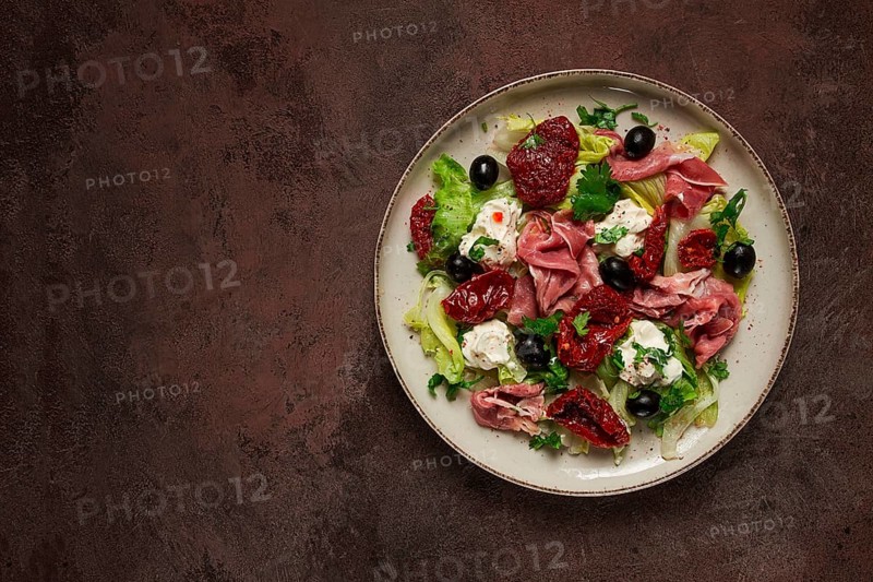 Salad with dried tomatoes, prosciutto, soft cheese, olives, homemade, top view