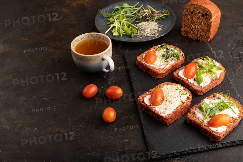 Red beet bread sandwiches with cream cheese, tomatoes and microgreen on black concrete background. Side view, copy space