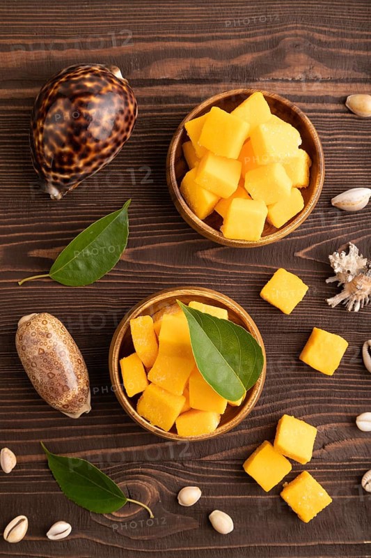 Dried and candied mango cubes in wooden bowls on brown wooden textured background. Top view, flat lay, close up, vegan, vegetarian food concept