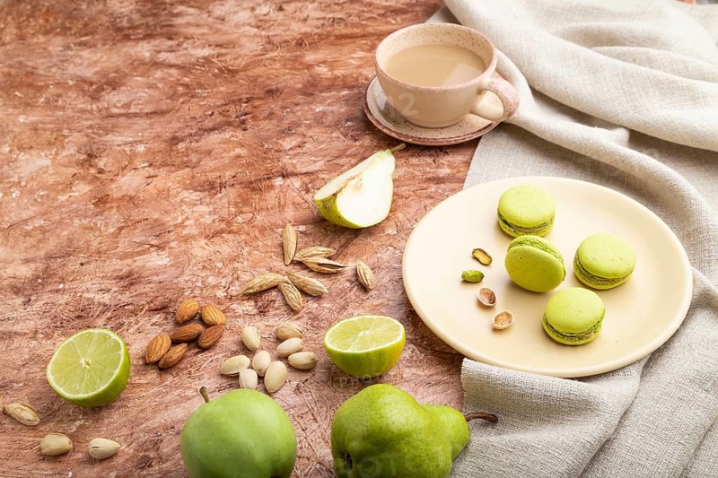 Green macarons or macaroons cakes with cup of coffee on a brown concrete background and linen textile. Side view, copy space