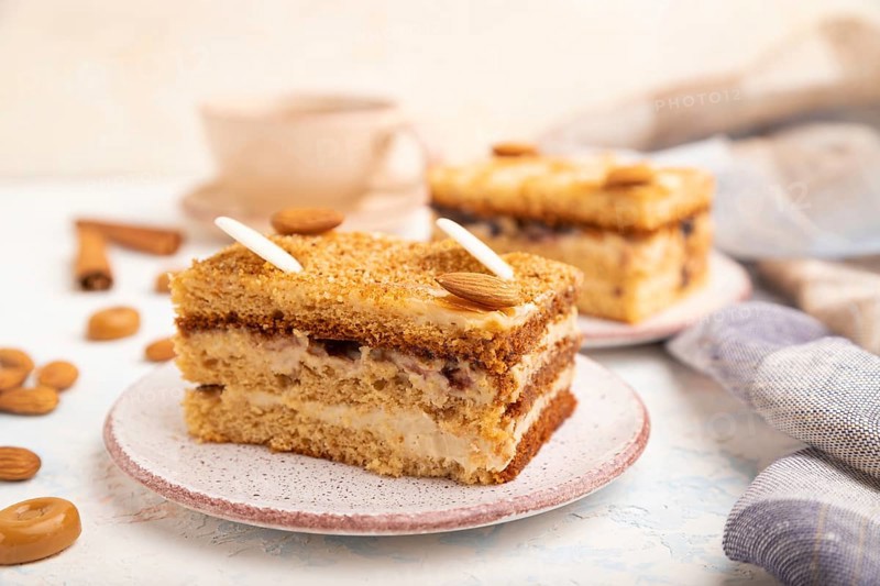 Honey cake with milk cream, caramel, almonds and a cup of coffee on a white concrete background and linen textile. Side view, selective focus, close up