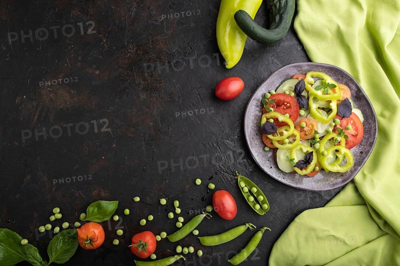 Vegetarian salad from green pea, tomatoes, pepper and basil on a black concrete background and green textile. top view, copy space, flat lay