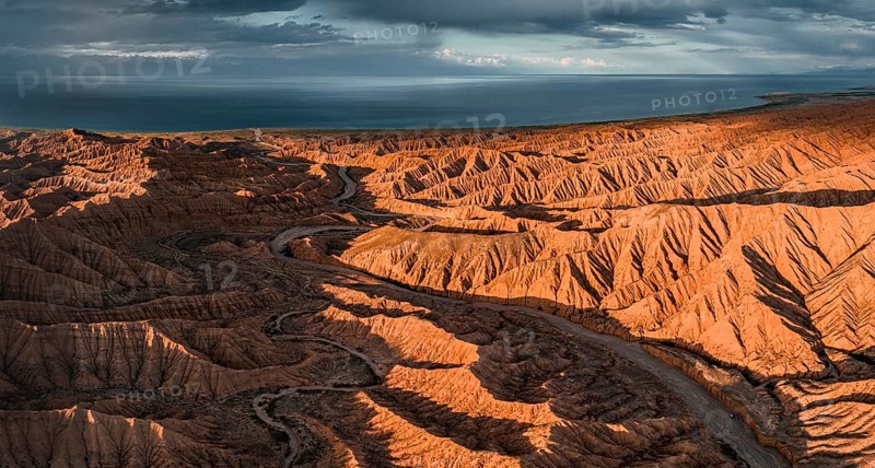 Riverbed runs through a landscape of eroded hills, badlands at sunset, Issyk Kul Lake in the background, aerial view, Canyon of the Forgotten Rivers, Issyk Kul, Kyrgyzstan, Asia