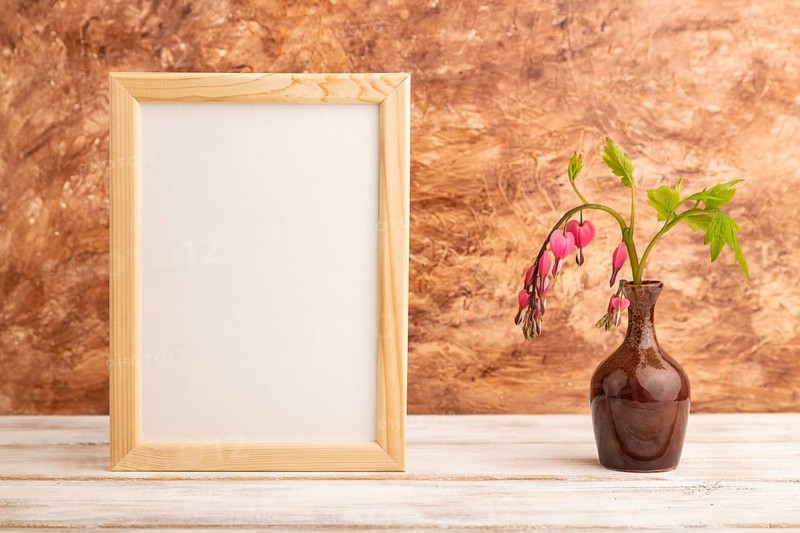 Wooden frame with pink dicentra, broken heart in ceramic vase on brown concrete background. side view, copy space, mockup, template, spring, summer minimalism concept