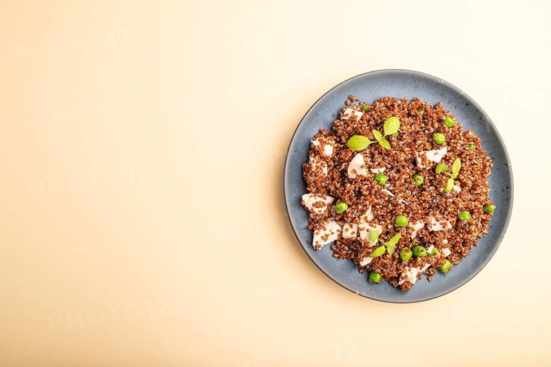 Quinoa porridge with green pea and chicken on ceramic plate on a pastel orange background. Top view, flat lay, copy space