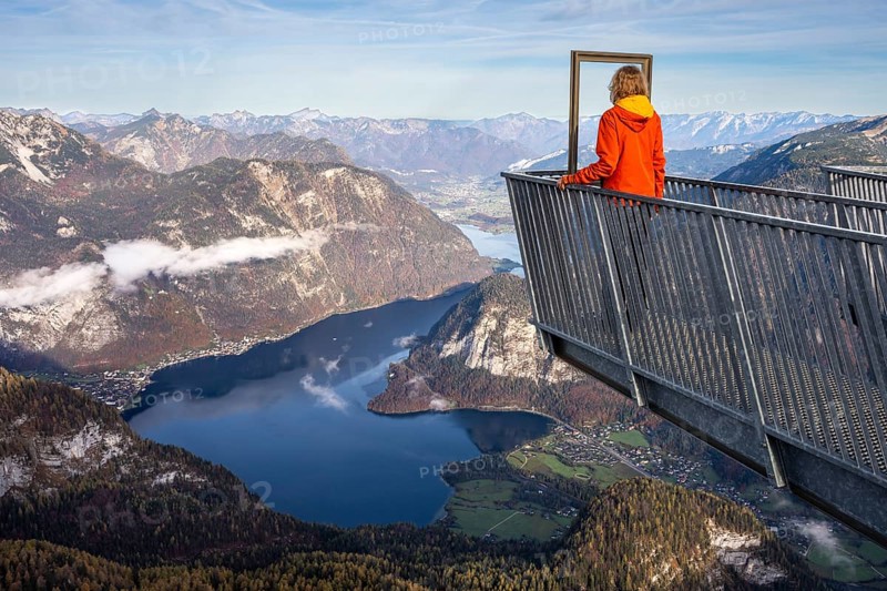 A hiker stands on the 5fingers viewpoint. View from the Dachstein Krippenstein to Lake Hallstatt. Hallstatt on the left, Obertraun on the right. Autumn, good weather. Some clouds in the mountains. Lake Hallstatt, Salzkammergut, Upper Austria, Austria, Europe