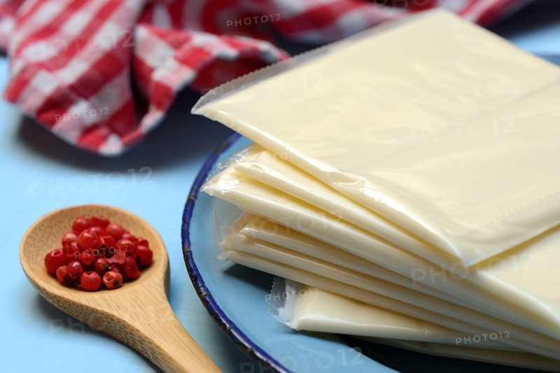 Processed cheese, slices of processed cheese wrapped in plastic and spoon with pink berries, red pepper