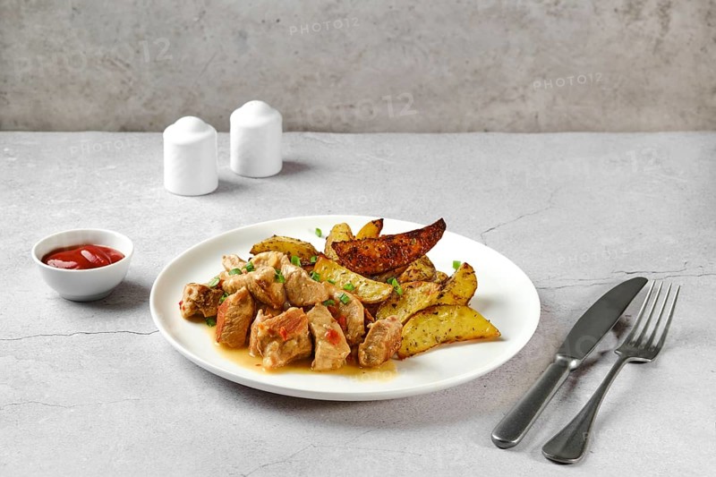 Beef goulash with baked potato wedges on a plate