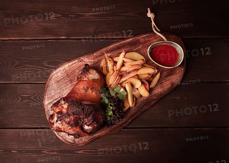 Pork knuckle, in soy-honey sauce, with fried potatoes, on a wooden chopping board, homemade, no people