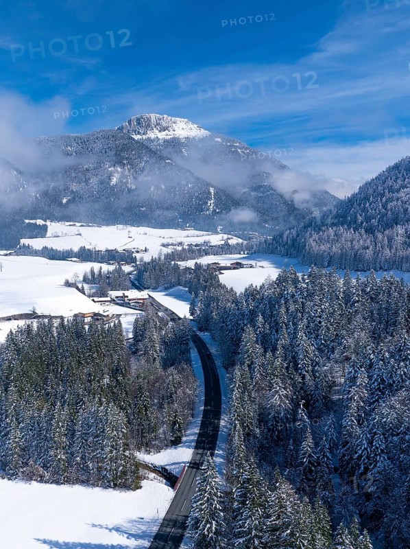 An idyllic snowy landscape with a road winding through the forest under a clear blue sky, Salzburger Land, Austria, Europe