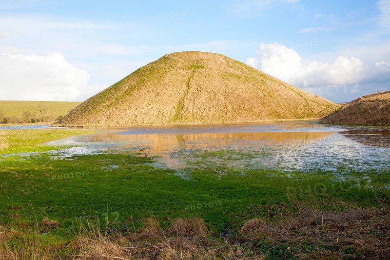 Silbury Hill ancient neolithic manmade chalk mound in Avebury, Wiltshire, England with flood water in the foreground