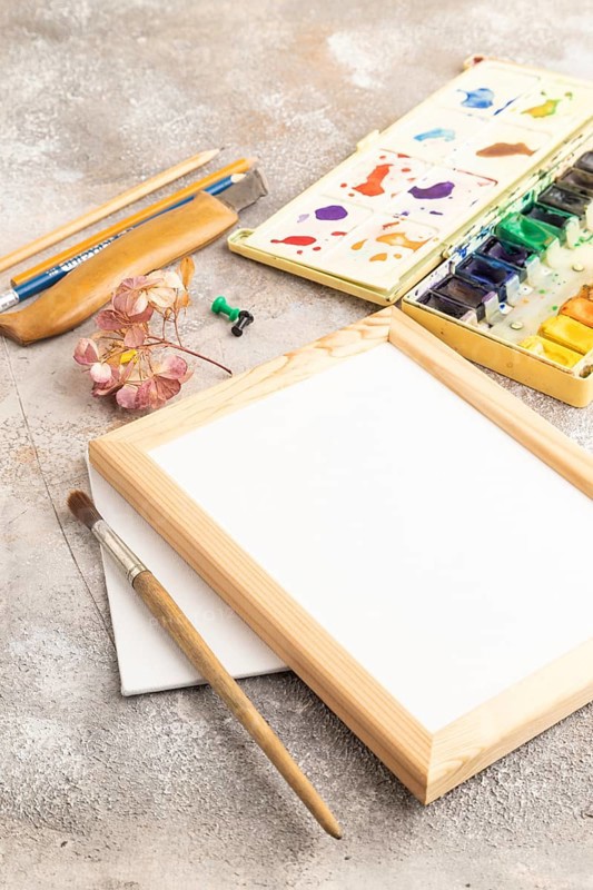 Drawing accessories set: brushes, pencils, watercolor, frame on brown concrete background. Side view, close up