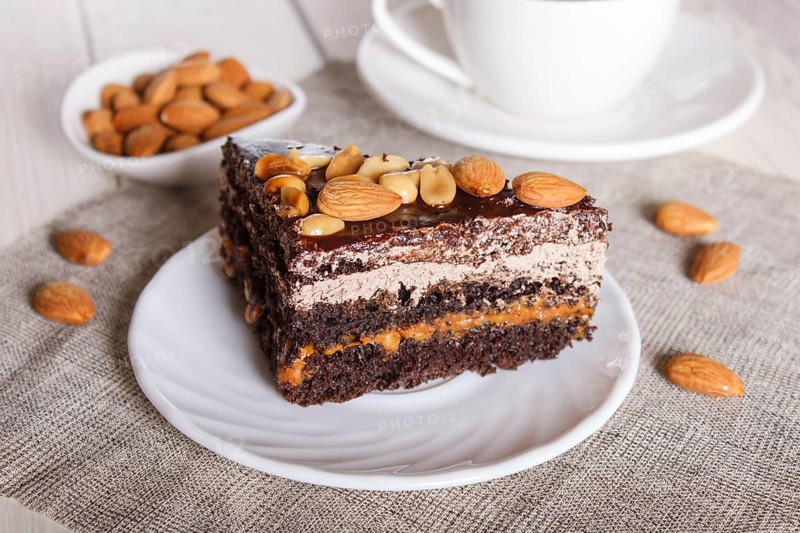 Chocolate cake with caramel, peanuts and almonds on a white wooden background. cup of coffee, close up, selective focus