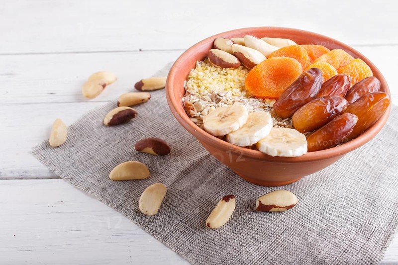 A plate with muesli, banana, dried apricots, dates, Brazil nuts on a white wooden background. close up. copy space