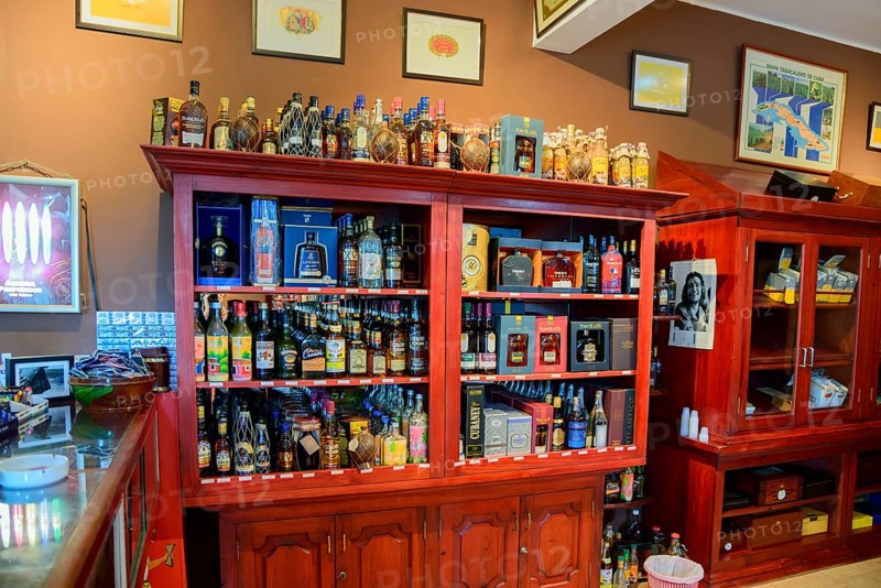 Inviting interior view of a bar with a selection of alcohol bottles on red wooden shelves and decorative interior, sale of spirits and cigars, Bayahibe, Dominican Republic, Hispaniola, Caribbean, America, Central America