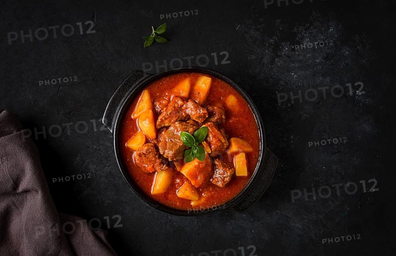 Stew with potatoes, in tomato sauce, with spices and herbs, close-up, no people, on a black background