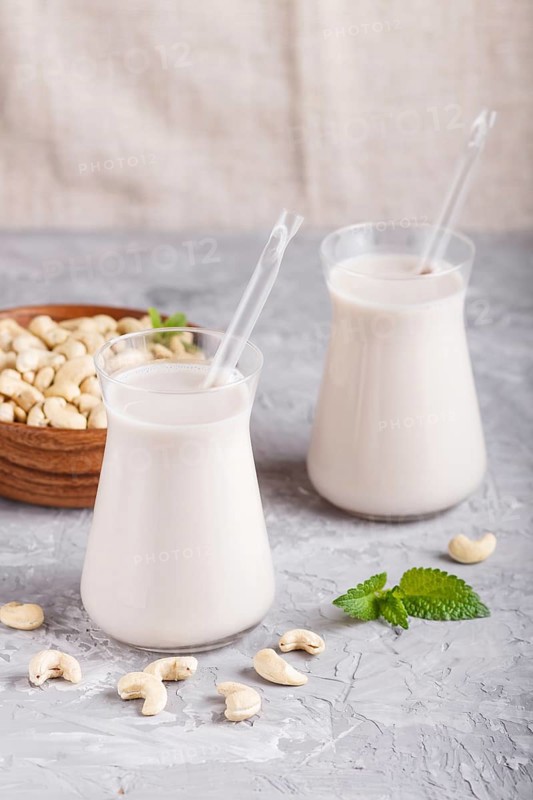 Organic non dairy cashew milk in glass and wooden plate with cashew nuts on a gray concrete background. Vegan healthy food concept, close up, side view