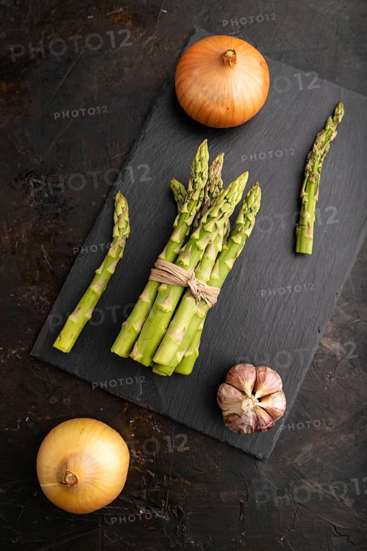Bunch of fresh green asparagus, garlic, onion on slate board on black concrete background. Top view, flat lay, close up. harvest, healthy, vegan food, concept