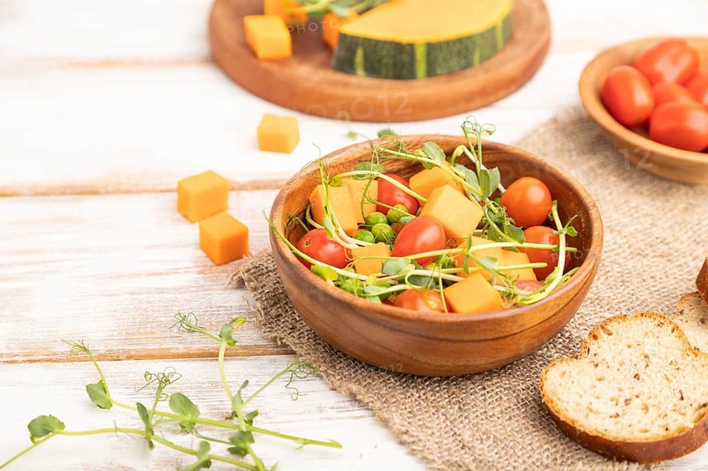 Vegetarian vegetable salad of tomatoes, pumpkin, microgreen pea sprouts on white wooden background and linen textile. Side view, close up, selective focus