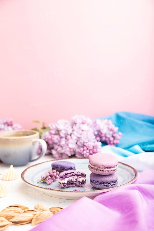 Purple macarons or macaroons cakes with cup of coffee on a white and pink background and magenta-blue textile. Side view, copy space, selective focus