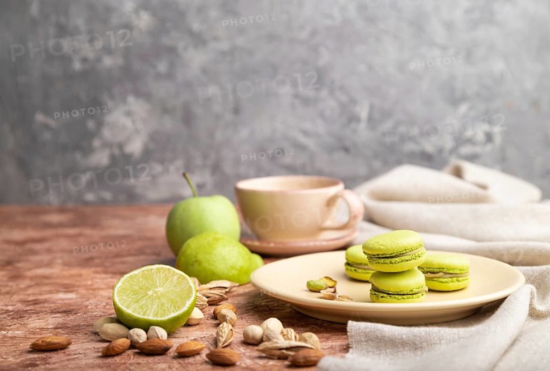 Green macarons or macaroons cakes with cup of coffee on a brown and gray concrete background and linen textile. Side view, copy space, selective focus