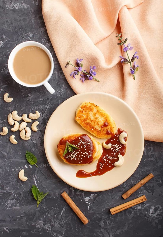 Cheese pancakes with caramel sauce on a beige ceramic plate and a cup of coffee on a black concrete background. top view, flat lay