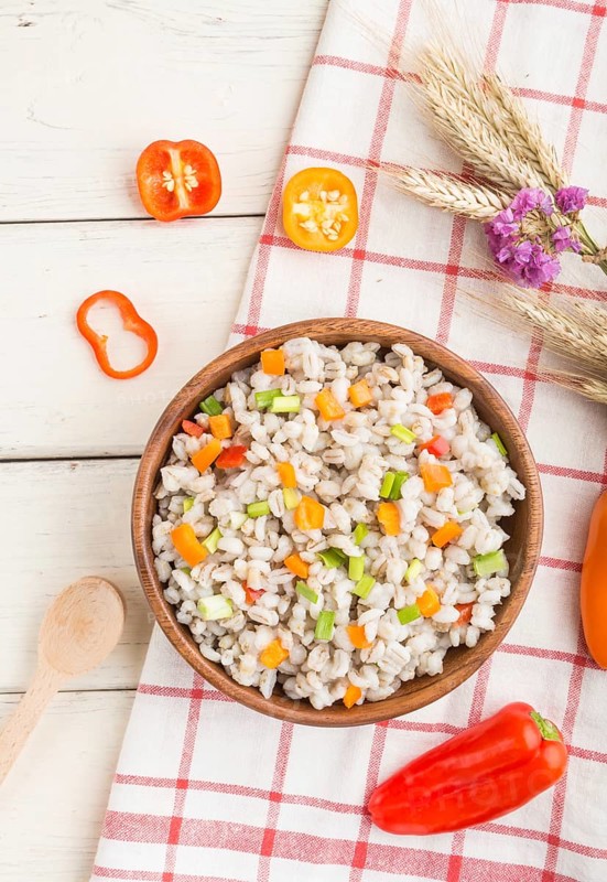 Pearl barley porridge with vegetables in wooden bowl on a white wooden background and linen textile. Top view, flat lay, close up. Russian traditional cuisine