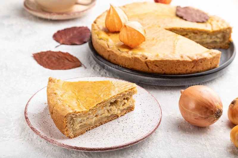Autumn onion pie decorated with leaves and cup of coffee on gray concrete background. Side view, close up