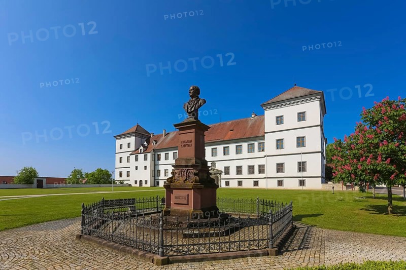 Monument in honour of Conradin Kreutzer, musician, conductor and composer, bust of Hans Baur, sculptor, sculpture, pedestal, writing, letters, public art, statue, behind Meßkirch Castle, Castle of the Counts of Zimmern, Zimmern Castle, regular four-wing castle complex, Renaissance building, architecture, historical building, park, castle garden, fence, blue sky, cloudless, Meßkirch, Sigmaringen district, Baden-Württemberg. Germany