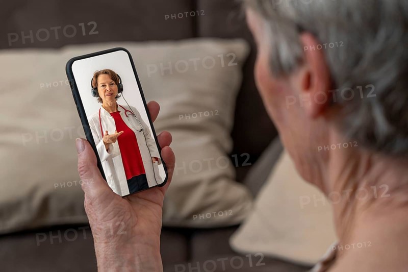 Symbolic image of telemedicine, patient speaks to a doctor in a video conference from home via mobile phone, smartphone