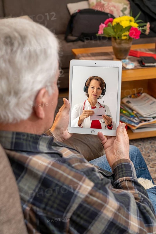 Symbolic image of telemedicine, elderly patient speaking to a doctor in a video conference from home