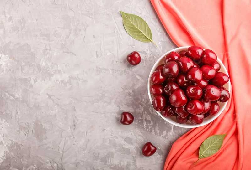 Fresh red sweet cherry in white bowl on gray background with red textile. top view, flat lay, copy space