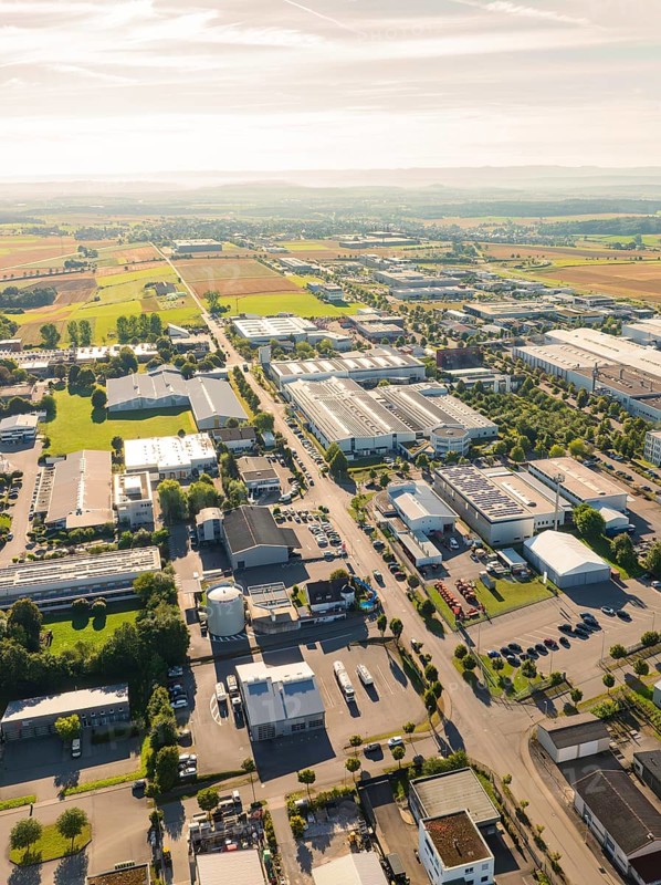 An industrial area with several factory buildings and neighbouring fields, seen from a bird's eye view in sunlight, Wolfsberg industrial area, Nagold, Black Forest, Germany, Europe
