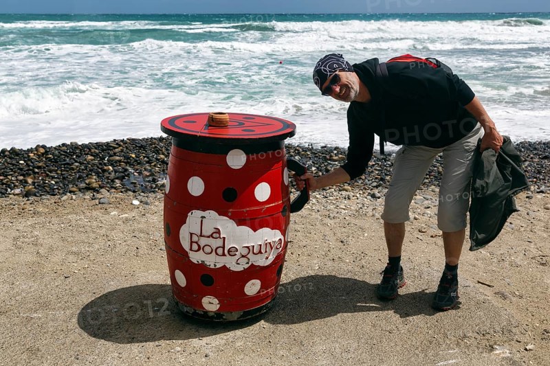 Red outdoor bar table, hiker, tourist holding jug, bar, beach bar, Cabo de Gata Natural Park, Cabo-de-Gata-Nijar, Las Negras, Almeria, Andalusia, Spain, Europe