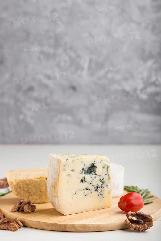 Blue cheese and various types of cheese with rosemary and tomatoes on wooden board on a white and gray background. Side view, copy space, selective focus