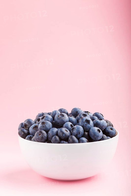 Fresh blueberry in white bowl on pink background. side view, copy space