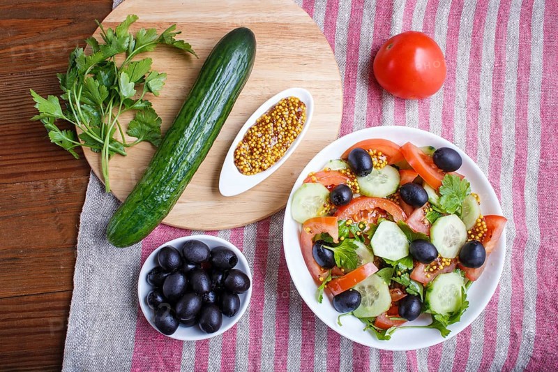 Vegetarian salad of tomatoes, cucumbers, parsley, olives and mustard on linen tablecloth, top view, flat lay