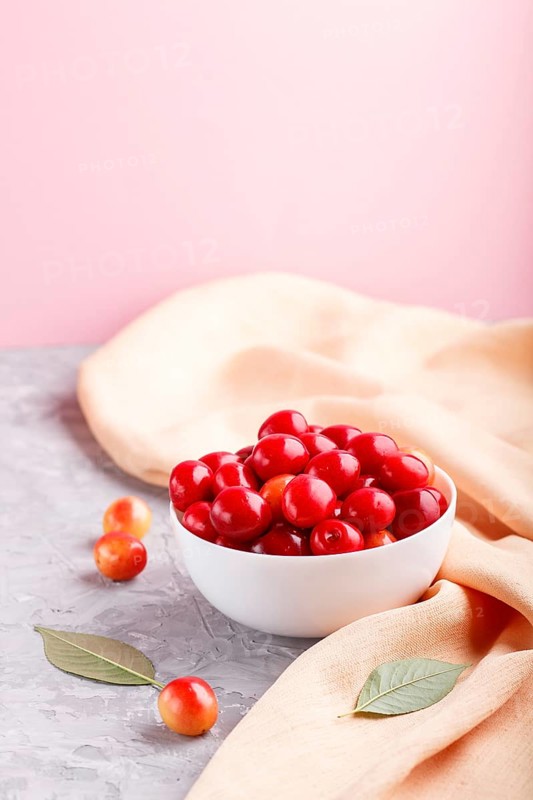 Fresh red sweet cherry in white bowl on gray and pink background with orange textile. side view, close up, selective focus, copy space