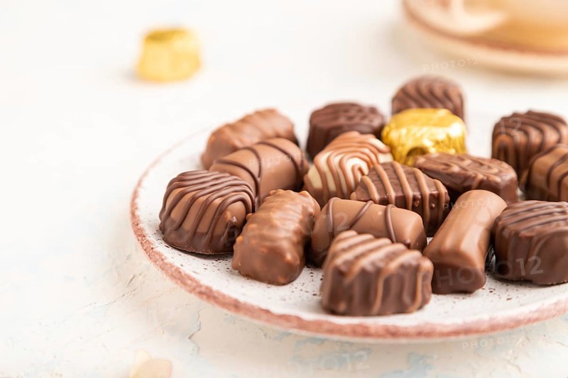 Chocolate candies with cup of coffee and hydrangea flowers on a white concrete background. side view, close up, selective focus
