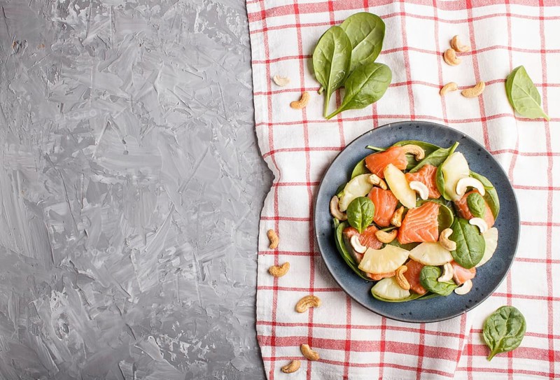 Fresh salmon with pineapple, spinach and cashew on a gray concrete background. Top view, copy space, flat lay, linen tablecloth